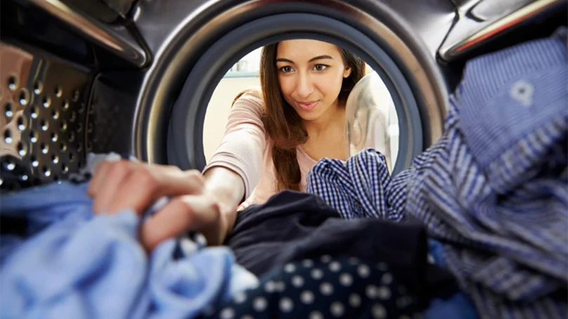 una imagen de una mujer metiendo ropa en la lavadora