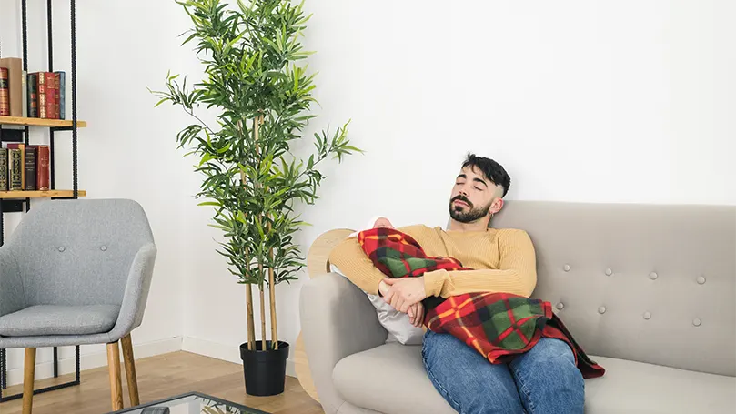 Imagen de un joven durmiendo en un sofá con un bebé.