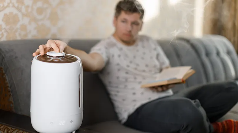 Un joven lee un libro en el sofá y prepara un humidificador