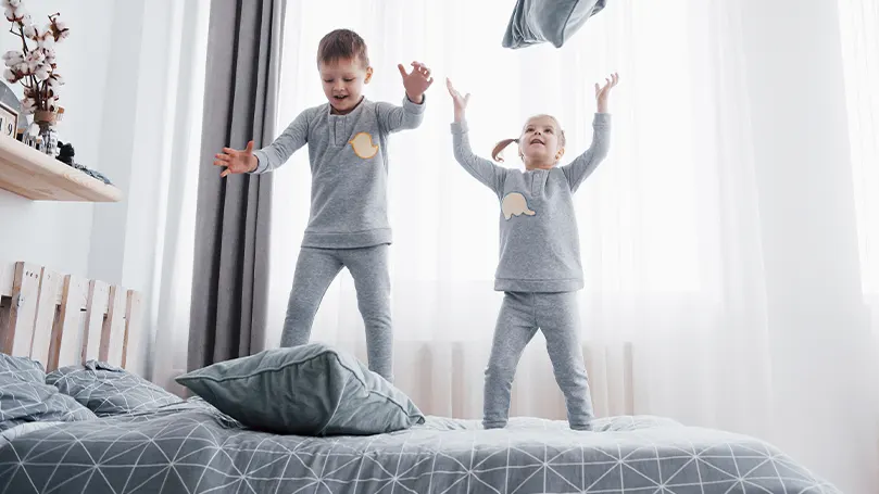 Una imagen de dos niños pequeños saltando sobre la cama.